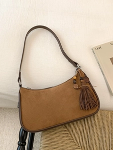 Brown suede hobo bag with tassel detail and silver hardware on white fabric background