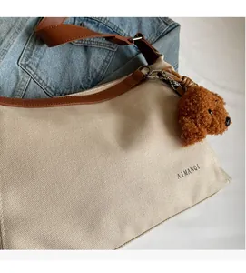 Detail of canvas tote bag with brown leather trim and cute plush teddy bear charm
