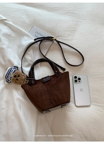 Detail der dunkelbraunen Wildleder-Beuteltasche mit Bärenanhänger und Metallplakette