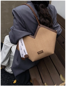 Close-up of woven tote bag showing herringbone texture, leather trim, and side strap detail