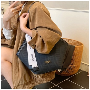 Detail of black tote bag with V-shaped woven texture and branded wide shoulder strap