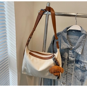Detail of off-white canvas crossbody bag with brown leather strap and plush charm