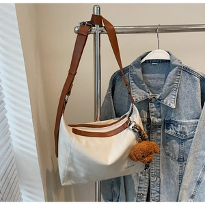 Close-up of cream canvas tote with brown leather strap and teddy bear charm