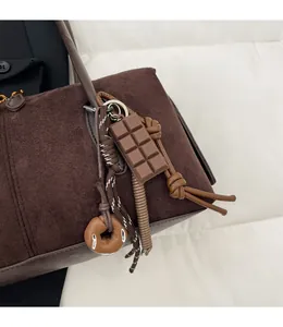 Gros plan de charms chocolat et donut suspendus à un sac à bandoulière en daim marron