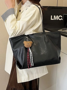 Minimalist black matte leather tote bag with a cute plush bear charm on a slim shoulder strap