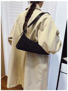 Detail of black suede shoulder bag with golden metal buckle and leather strap on model