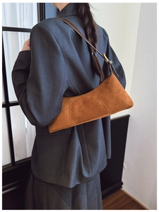 Detail of brown suede shoulder bag featuring retro vertical seams and leather strap
