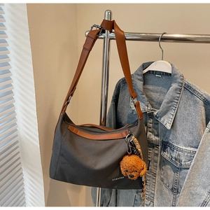 Detail of dark grey canvas tote bag with brown leather strap and cute bear charm