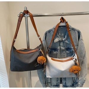 Detail of hobo shoulder bags in grey and cream with leather straps and bear pendant
