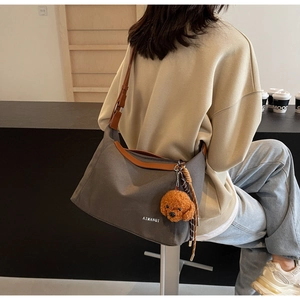 Detail of dark grey canvas tote bag with brown leather trim and a cute teddy bear charm