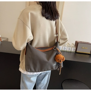 Close-up of crescent canvas tote bag with brown leather trim and cute teddy bear charm