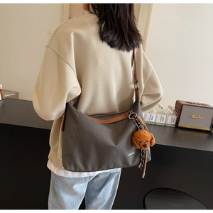 Detail of grey canvas tote bag with brown leather straps and a plush bear pendant