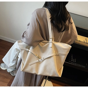 Detail view of large cream PU leather tote bag worn by a model in a cozy indoor setting