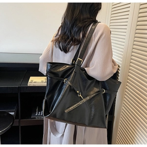 Detail of high-gloss black tote bag with adjustable gold buckle on a shoulder strap
