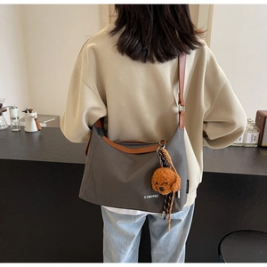 Detail of gray canvas hobo bag with leather trim and cute brown dog plush pendant