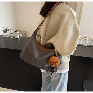 Detail of grey canvas tote with brown leather trim and a cute plush bear charm attached