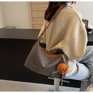 Detail view of large grey canvas crossbody bag with brown leather trim and bear pendant