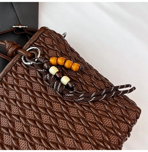 Detailed view of dark brown woven leather bucket bag with wooden bead charm and silver D-ring