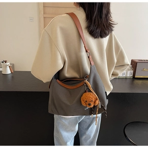 Detail of canvas tote bag with brown leather straps and cute plush dog pendant