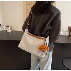 Model wearing a beige canvas tote bag with brown leather strap in a minimalist cafe setting