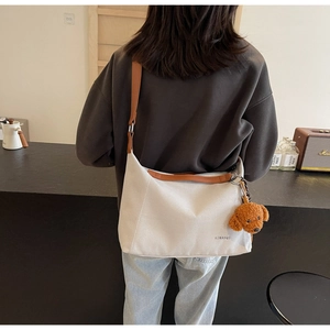 Detail of canvas tote bag with brown leather straps and cute plush bear accessory