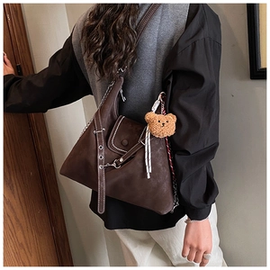 Detail of dark brown suede shoulder bag with contrast stitching and plush bear charm