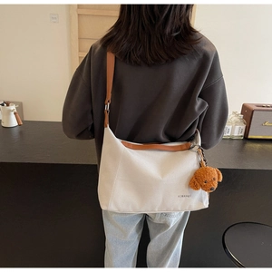 Detail of canvas tote bag featuring brown leather trim and cute teddy bear charm