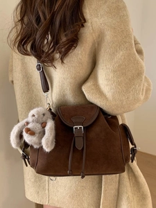 Brown suede bucket bag with plush rabbit charm worn by a model in a warm winter setting