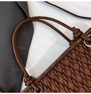 Detail of dark brown woven bucket bag featuring intricate leather texture and knotted handle
