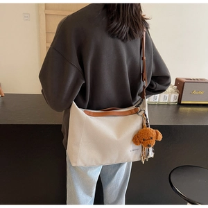 Large beige canvas tote bag with brown leather trim and a cute teddy bear charm