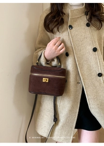 Détail du sac boîte en daim marron foncé porté avec un manteau en laine beige en intérieur