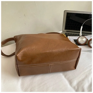 Détail du sac seau en cuir marron avec doubles surpiqûres blanches et texture grainée