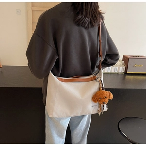 Detailed shot of white canvas tote bag with brown leather straps and teddy bear pendant