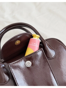 Detail of dark brown glossy leather handbag showing the front pocket with metal closure