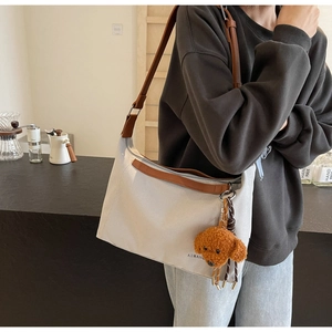 Detail of white canvas tote with brown straps and a cute teddy bear plush charm