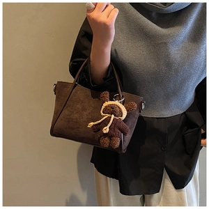 Detail einer braunen Wildleder-Beuteltasche mit süßem Teddybär-Anhänger am Griff