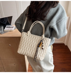 Detail of woven bucket bag featuring wooden bead tassel and textured leather surface