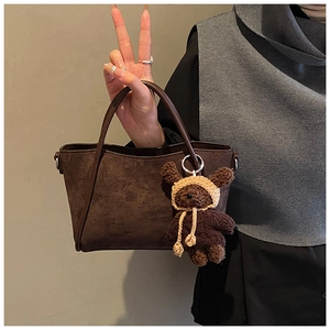 Detail einer dunkelbraunen Wildleder-Beuteltasche mit langen Griffen und Teddybär-Anhänger