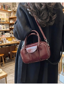 Detail of burgundy glossy leather bowling bag featuring double handles and a shoulder strap