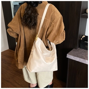 Détail d'un grand sac hobo crème avec boucles dorées porté par un mannequin en intérieur