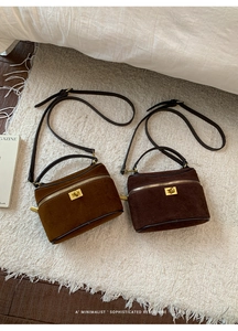 Deux sacs boîtes en daim caramel et marron foncé posés sur un tapis blanc texturé