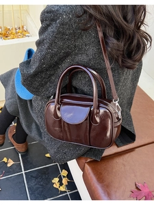 Detail of dark brown glossy leather bowling bag held by a person over an autumn background