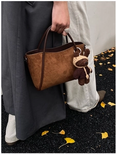 Nahaufnahme der braunen Wildleder-Beuteltasche mit Strickbär-Anhänger und Lederriemen