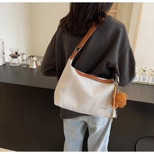 Detail of canvas tote bag featuring brown leather straps and a cute plush bear charm