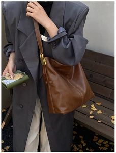 Détail d'un sac seau en cuir marron foncé avec coutures contrastées blanches et finitions dorées