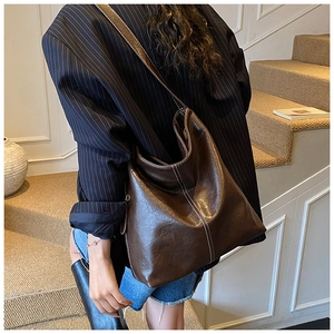 Détail du sac cabas en cuir marron foncé avec coutures blanches et silhouette hobo
