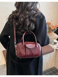 Close-up of a burgundy oil-wax leather bowling bag worn as a shoulder bag in a cafe