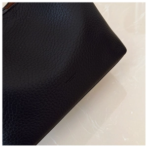 Close-up of black lychee grain leather with embossed MUCODIU BAG logo on the side