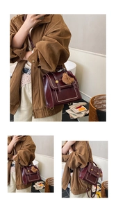 Detail of dark red vintage crossbody bag with white stitching and plush bear charm