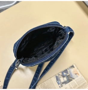 Detail of blue denim crossbody bag showing the main zipper opening and black lining